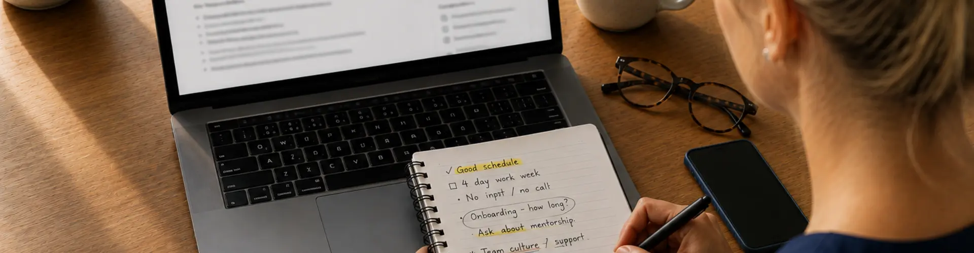 Healthcare professional in navy scrubs reviewing a healthcare job posting on a laptop while taking handwritten notes to evaluate the opportunity before applying.