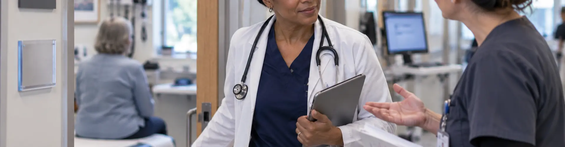 Experienced advanced practice provider pauses outside a patient exam room to assist a colleague.
