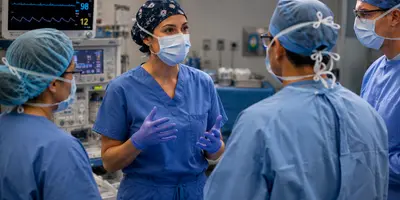 CRNA leading a collaborative preoperative discussion with surgeons and operating room staff in a modern surgical suite.