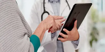Nurse practitioner using digital healthcare technology while consulting with an elderly patient, illustrating the expanding role of nurse practitioners in modern healthcare.